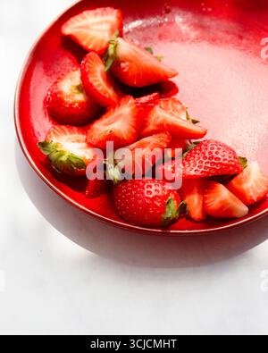 Saftige, frische Erdbeeren sind auf einem leuchtend roten Teller angeordnet und bilden einen auffälligen Kontrast. Die leuchtenden Farben und die frischen Produkte machen dieses Hotel zu einem verlockenden Erlebnis Stockfoto