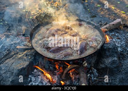 Verkäufer Braten Tintenfische zum Verkauf in Pflanzenöl in einer großen Pfanne über offenem Feuer auf einem lokalen Straßenmarkt auf der Insel Sansibar, Tansania, Stockfoto