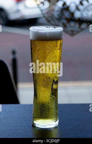 Nahaufnahme eines hohen, schwitzenden Glases Bier mit einem schäumenden Kopf und aufsteigenden Blasen, die auf einem dunklen Tisch sitzen. Stockfoto