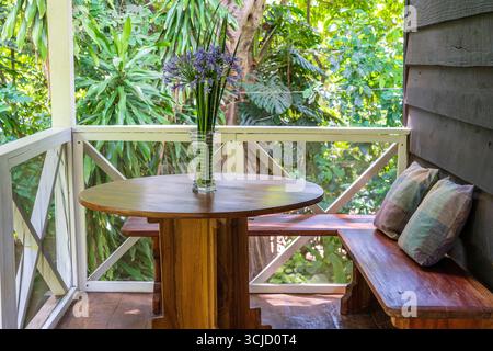 Holzbank mit Kissen und Tisch mit einer Blumenvase auf einer Holzveranda, Tansania, Ostafrika, Nahaufnahme Stockfoto