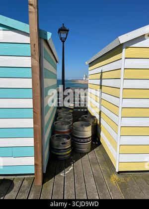 Farbenfrohe gestreifte Hastings Pier Hütten mit Bierfässern und alter Lampe, klarer blauer Himmel Stockfoto