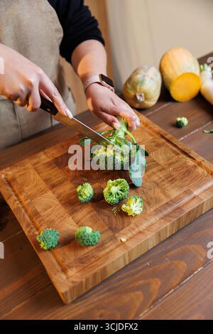 Frischer Brokkoli wird auf einem hölzernen Schneidebrett in gemütlicher Küche geschnitten Stockfoto