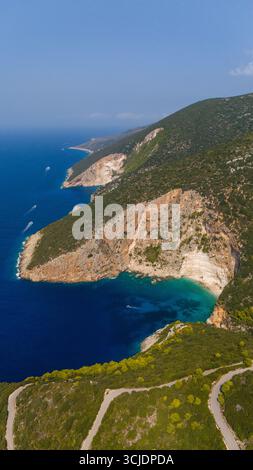 Dramatische Küste mit felsigen Klippen, smaragdgrünem Wasser, tiefblauem Ozean und geschwungener Hangstraße umgeben von dichtem grünen Wald von oben gesehen Stockfoto