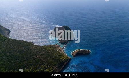 Luftbild der Höhleninsel Agios Andreas, die schroffe Klippen, türkisfarbenes, seichtes, tiefes Ozeanwasser und dichte grüne Vegetation zeigt, die die Hügel bedeckt Stockfoto