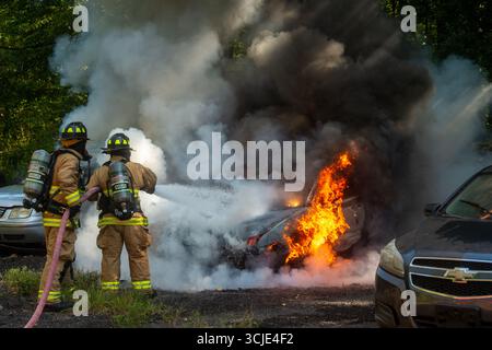 Feuerwehrleute bekämpfen ein brennendes Autofeuer mit starkem Rauch und Flammen und zeigen Notfallmaßnahmen, Brandschutz und dramatische Rettungsaktionen. Stockfoto