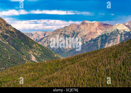 Ein majestätischer Panoramablick auf eine riesige Berglandschaft unter einem strahlend blauen Himmel mit beeindruckenden horizontalen weißen Wolken. Der Vordergrund wird dominiert b Stockfoto
