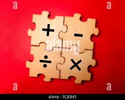 Das Bild zeigt vier hölzerne Puzzleteile, die zusammen ein Quadrat bilden. Jedes Stück verfügt über ein anderes Symbol für die arithmetische Grundoperation. Stockfoto