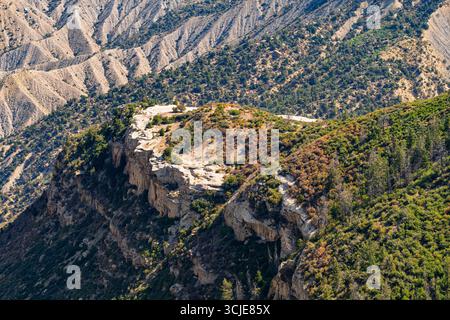 Ein weitläufiger Hochwinkel zeigt eine dramatische, trockene Berglandschaft bei hellem Sonnenlicht. In der Mitte befindet sich eine markante felsige mesa oder Klippe Stockfoto