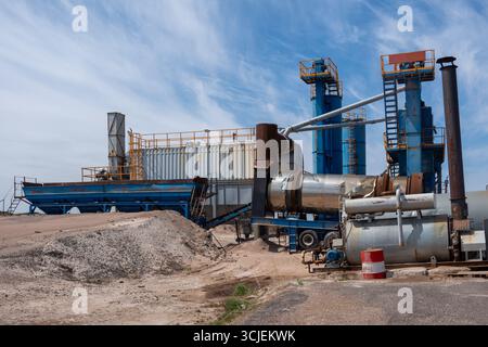 Große industrielle Asphaltmischanlage mit blauen Maschinen und Förderern, erfasst an einem sonnigen Tag mit Himmelshintergrund, repräsentiert Bauarbeiten Stockfoto
