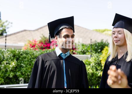 Absolventen in Mützen und Kleidern feiern im Freien, lächeln und genießen Momente Stockfoto