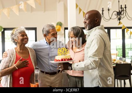 Anlässlich des Geburtstags lächelte eine Gruppe von Senioren mit Kuchen im dekorierten Zimmer Stockfoto