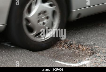 EMBARGOED BIS 0001 MONTAG, 8. SEPTEMBER Aktenfoto vom 11. November 05/18 eines Autos, das auf einer Straße ein Schlagloch trifft. Räte, die nur wenig oder gar keine Schlaglochprävention durchführen, sollten sich einer obligatorischen Schulung unterziehen, so wurde behauptet. Der RAC forderte die Regierung auf, die Maßnahme einzuführen, da der "reaktive" Ansatz vieler lokaler Behörden "eindeutig" zum "schlechten Zustand" vieler Straßen beigetragen hat. Ausgabedatum: Montag, 8. September 2025. Stockfoto