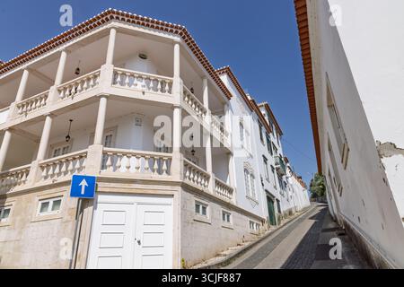 Eine charmante, bergauf gelegene Straße in Torres Novas, Portugal, gesäumt von traditionellen weißen Gebäuden und einem verzierten Balkon unter klarem blauen Himmel. Stockfoto