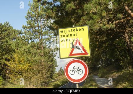 Gelbes Hirsch, das Verkehrswarnschild überquert und kein Fahrrad erlaubt auf einer Landstraße Stockfoto