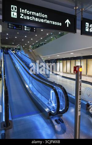 Beleuchteter Flughafen Zürich mit Escalator und Schild in Bewegung bei Nacht im Flughafen Kloten, Zürich, Kanton Zürich, Schweiz Stockfoto