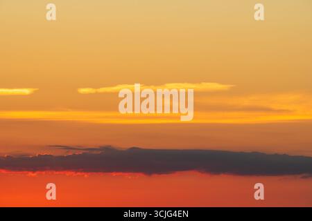 Lebendiger, farbenfroher Sonnenuntergang-Himmel mit einem warmen orange-roten Farbverlauf, mit Schichten dunkler und leuchtender Wolken. Stockfoto