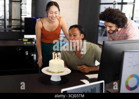 Kollegen feiern Geburtstag im Büro, Mann, der Kerzen auf Kuchen bläst Stockfoto