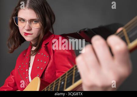 Die verspielte Gitarristin genießt es, Gitarre zu spielen, und sie tut das mit ihren Lippen. Leidenschaftliche junge Frau, die eine Brille trägt, IS Stockfoto
