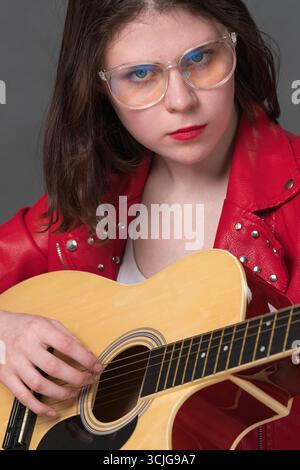 Nahaufnahme einer Gitarristin, die ihr akustisches Musikinstrument mit Streichern bespielt und in die Kamera blickt Stockfoto