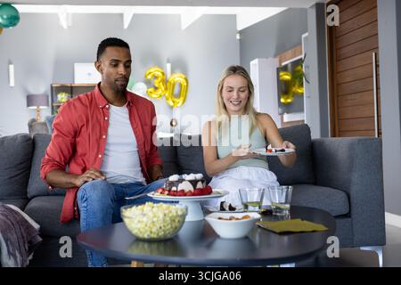 Freunde genießen Snacks und Kuchen zu Hause während der Geburtstagsfeier Stockfoto