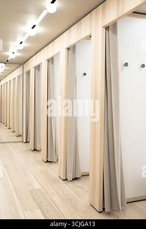 Gut beleuchtete Ankleide- und Umkleideräume zum Anprobieren von Kleidung in einem Geschäft mit Holzrahmen und beigefarbenen Textilvorhängen in einem modernen Geschäft Stockfoto