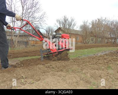 Roter Metallpflug bei der Arbeit auf dem Bauernhof Pflügen von Boden, Anbauflächen von Ackerland mit manueller mechanischer persönlicher Ausrüstung, Pflugmannarbeit Stockfoto