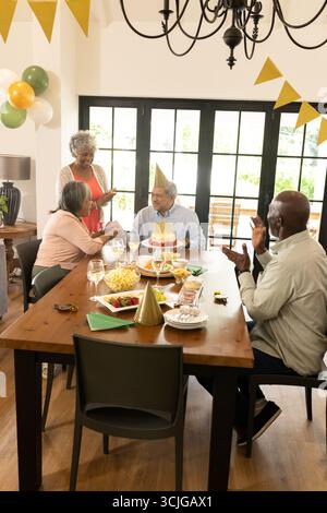 Familie feiert zu Hause Geburtstag, Seniorenmann trägt Partyhut und lächelt Stockfoto