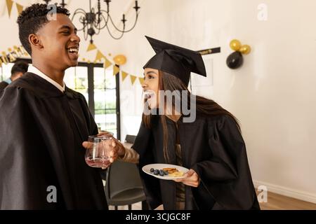 Absolventen in Mützen und Kleidern feiern mit Snacks und Getränken auf der Party Stockfoto