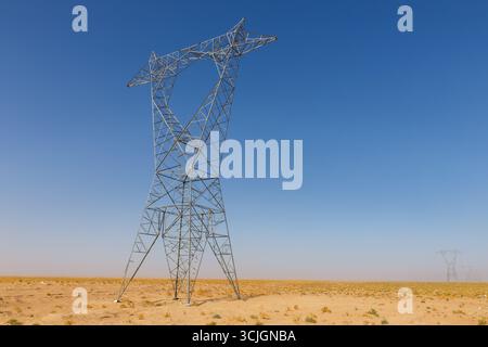 Ein Hochspannungs-Pylon steht in der weiten, trockenen Wüste Afghanistans unter einem klaren blauen Himmel. Stockfoto