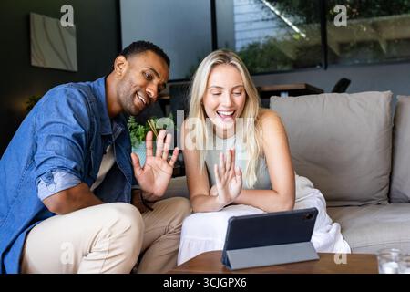 Lächelnde Freunde, die zu Hause auf einem Tablet chatten, winken und Gespräche genießen Stockfoto