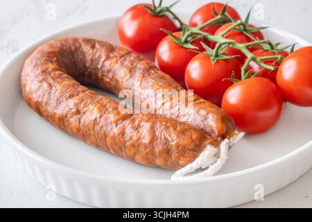 Eine einzelne Wurst und frische Tomaten, einfach auf einem hellen, sauberen Hintergrund Stockfoto