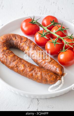 Eine einzelne Wurst und frische Tomaten, einfach auf einem hellen, sauberen Hintergrund Stockfoto