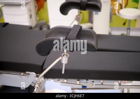 Detaillierte Ansicht eines schwarzen gepolsterten medizinischen Bügels mit Riemen, der an einem Untersuchungs- oder Operationstisch in einem Krankenhaus befestigt ist. Stockfoto