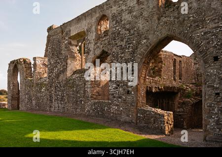 Das alte Steingebäude hat viele Fenster und einen großen Torbogen. Der Bogengang ist offen und das Gebäude ist von Gras umgeben. Das Gebäude scheint es zu sein Stockfoto