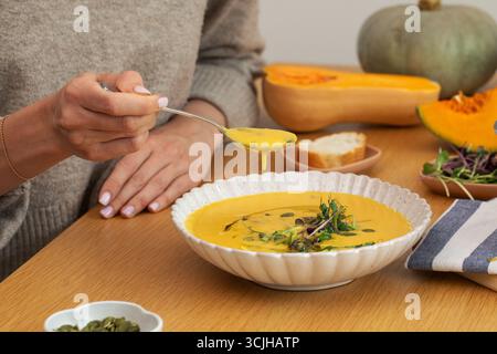 Frau isst Kürbissuppe am Holztisch. Gesunde und vegane Mahlzeiten. Stockfoto