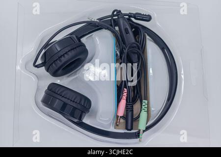 Schwarzes kabelgebundenes Headset mit Mikrofon in Kunststoffverpackung auf weißem Studio-Hintergrund. Stockfoto