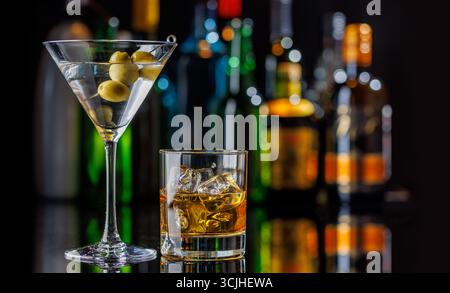 Martini Cocktail und Whiskey auf den Felsen auf einem Bartisch. Das farbenfrohe Bokeh der beleuchteten Flaschen im Hintergrund verbessert die Stimmung und sorgt für einen Dye Stockfoto