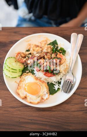 Nahaufnahme einer Frau im Restaurant, die tagsüber ein thailändisches Basilikum-Meeresfrüchte-Gericht mit Spiegelei und Reis im Restaurant isst Stockfoto