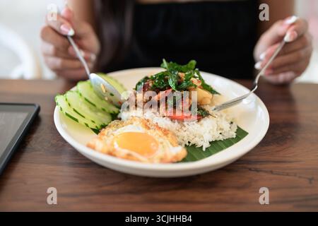 Nahaufnahme einer Frau im Restaurant, die tagsüber ein thailändisches Basilikum-Meeresfrüchte-Gericht mit Spiegelei und Reis im Restaurant isst Stockfoto