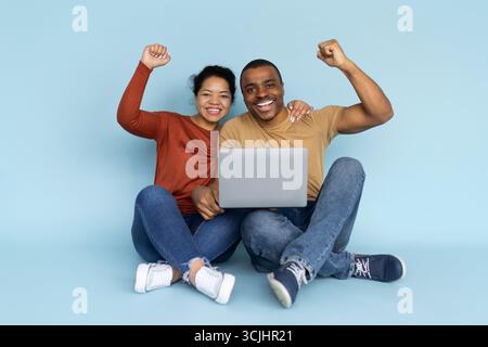 Aufgeregt afroamerikanisches Paar sitzt mit Laptop und jubelt vor Freude Stockfoto