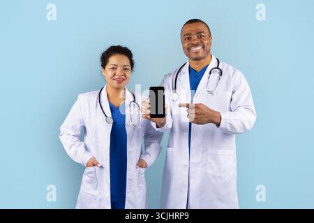 Lächelnde afroamerikanische Ärzte im Studio zeigen Smartphone zur Kamera Stockfoto