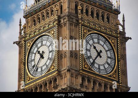 Der berühmte Big Ben Uhrenturm vor einem blauen Himmel: Eine detaillierte Nahaufnahme von Londons berühmtem Wahrzeichen, das seinen komplizierten goldenen und verwitterten Stein betont Stockfoto