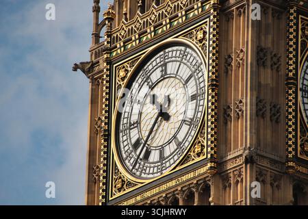 Der berühmte Big Ben Uhrenturm vor einem blauen Himmel: Eine detaillierte Nahaufnahme von Londons berühmtem Wahrzeichen, das seinen komplizierten goldenen und verwitterten Stein betont Stockfoto