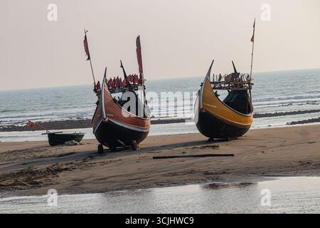 Hell bemalte hölzerne Fischerboote, bereit für die Seereise unter dem sanften goldenen Morgenlicht des Coxs Bazar Stockfoto