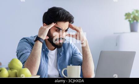 Gestresste arabische männliche Unternehmer Probleme bei der Arbeit, sitzen aufgeregt mit Laptop-Computer am Küchentisch Stockfoto