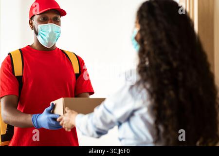 Schwarzer Lieferer in medizinischer Maske, der der Frau eine Schachtel gab Stockfoto