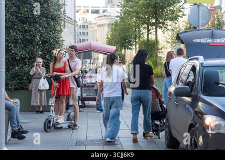 Moskau, Russland, 25. August 2025, Junges Paar mit einem Roller auf einer lebhaften Moskauer Straße. Stockfoto