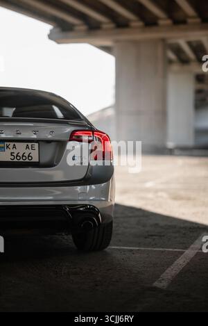 Silberner Volvo S60 unter einer Brücke bei Sonnenuntergang. Rückansicht der schwedischen Sportlimousine gegen die Sonne, Betonsäulen links. Stockfoto