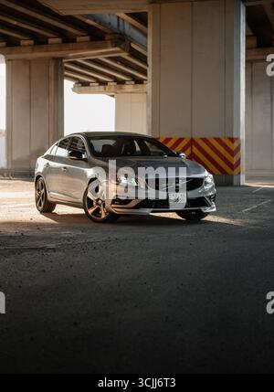 Der silberne Volvo S60 parkt unter einer Brücke. Vorderansicht der schwedischen sportlichen Limousine in Sonnenstrahlen, Betonbrückensäulen hinten Stockfoto