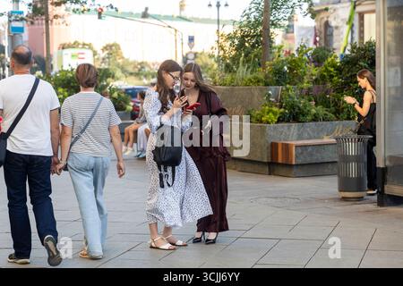 Moskau, Russland, 25. August 2025, Junge Frauen, die auf einer Moskauer Straße auf ihre Handys schauen. Stockfoto